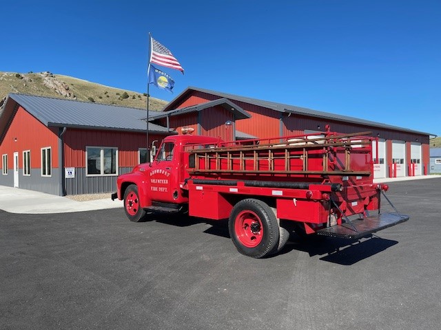 1954 Drummond Fire Truck Exterior Restored; parked in front of Drummond Fire Hall with American Flag blowing in background on Fire Hall